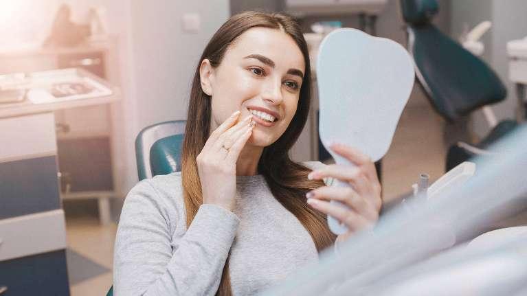 woman looking at smile in mirror while sitting in dental chair